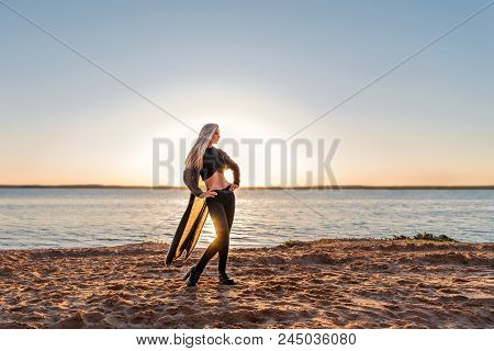 Attractive Athletic Girl Posing Standing On A Sandy Beach In The Rays Of The Setting Sun
