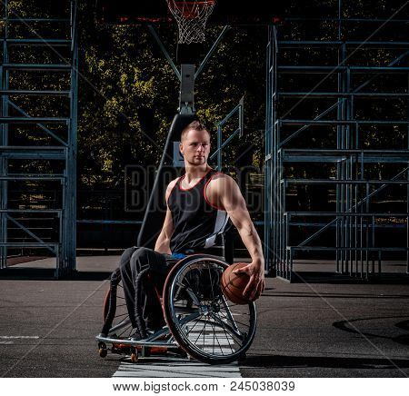 Cripple Basketball Player In A Wheelchair Holds A Ball On Open Gaming Ground.