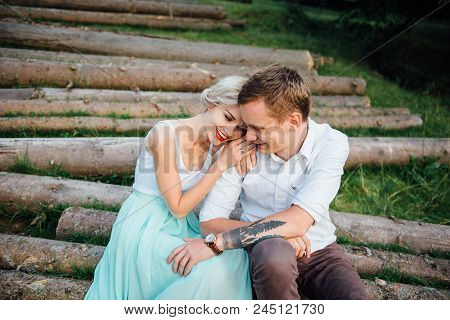 Couple In Love Walking Near Logs In The Mountains.
