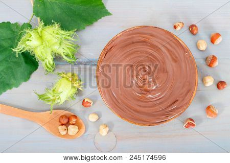 Sweet Chocolate Hazelnut Spread With Whole Nuts, Wooden Spoon And Green Hazelnut On Blue Table.