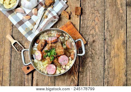 Top View Of Old Saucepan With Garlic Soup, Fresh Garlic Bulbs, Cloves, Colored Pepper, Wooden Spoon,