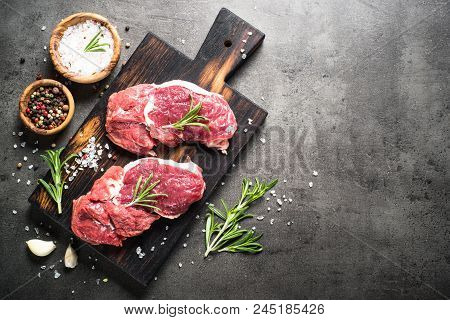 Fresh Meat. Raw Beef Steak On A Cutting Board With Rosemary And Spices On Dark Stone Table. Top View