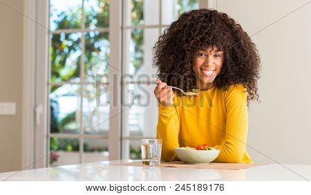 African american woman eating pasta salad with a happy face standing and smiling with a confident smile showing teeth