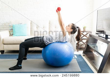 Fit Young Hispanic Woman Leaning Over A Stability Ball And Doing Hands Work Out With Weights