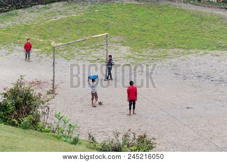 GHALEGAUN, NEPAL - CIRCA MAY 2018: chidren play football, one of them carry a blue basin on his head. The goal is made of tree branches.