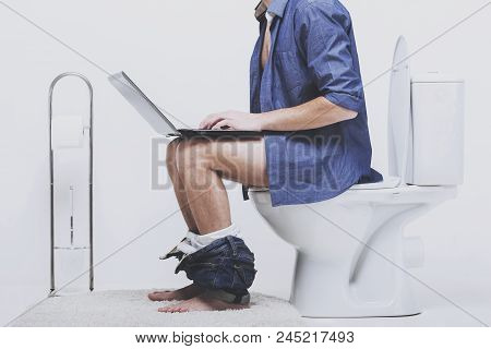 Man Is Working With Laptop While Sitting On Toilet. Sitting In Wc With Downtrodden Pants.