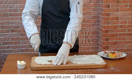 Chef Hads Slicing Dough Sheet With Roller Knife. Close Up