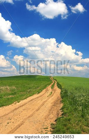 Dusty Country Road Passing Through The Fields And Meadows