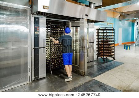Confectionery Manufacturing. Baker Puts Cookies Into Oven For Baking.