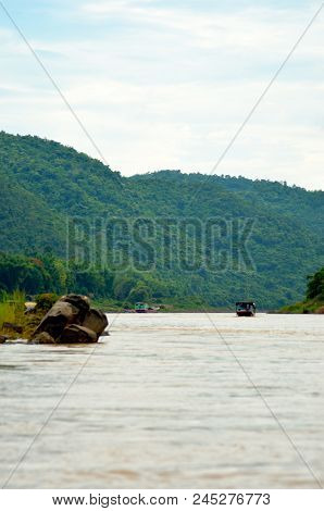 Two Wooden Boats Are On The Meking In Laos. The Water Is Muddy. On Either Side Are Hills Covered Wit