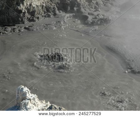Bubbling Mud In A Mud Pool. Steam Is Rising From The Mud. The Surrounding Rocks Are Tinged Yellow Fr