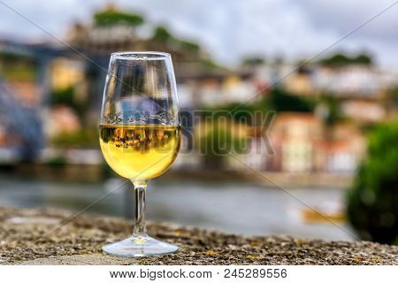 Glass of port wine on an old stone wall at an outdoor restaurant with the Douro river  and Dom Luis I bridge blurred in the background in Porto, Portugal