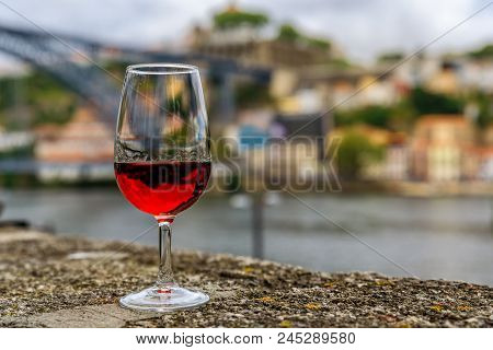 Glass of port wine on an old stone wall at an outdoor restaurant with the Douro river  and Dom Luis I bridge blurred in the background in Porto, Portugal