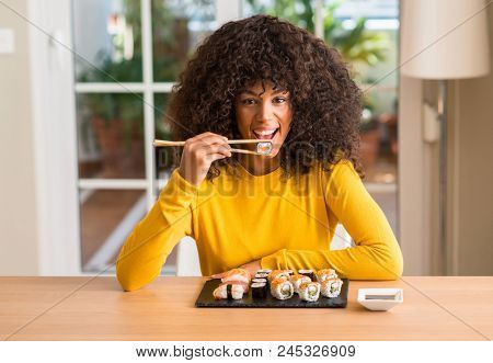 African american woman eating sushi using chopsticks at home with a confident expression on smart face thinking serious