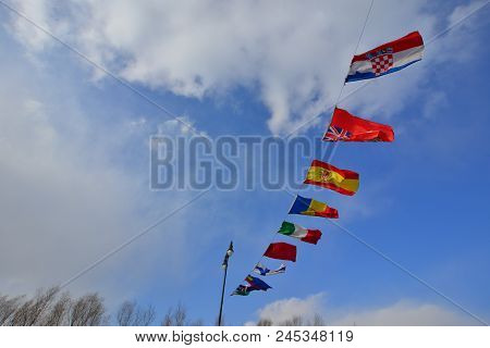 Flags Of Different Countries Flapping In Wind Against Blue Sky.