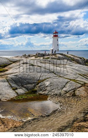 The Lighthouse In The Village Of Peggys Cove, Nova Scotia, Canada As Tourists Climb On The Rock Foun