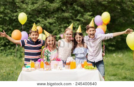 holidays, childhood and celebration concept - happy kids hugging on birthday party at summer garden