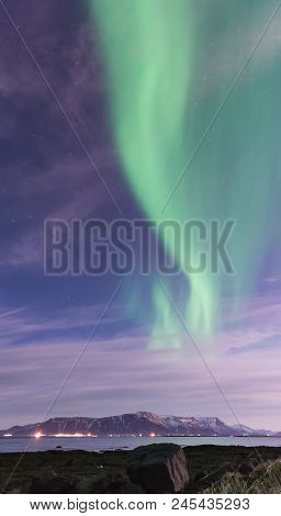 Swirl Of Green Aurora Borealis Over A Black Sand Beach, The Ocean, And Mountains Outside Reykjavik, 