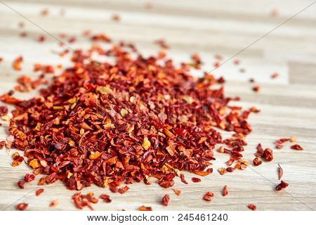 Pile Of Dried Red Hot Chilly Flakes On Light Wooden Background, Top View, Close-up, Macro, Shallow D