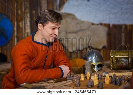 Portrait Of Man In Russian Ethnic Suit Playing Board Game Like Chess. Folk, Competition And Traditio