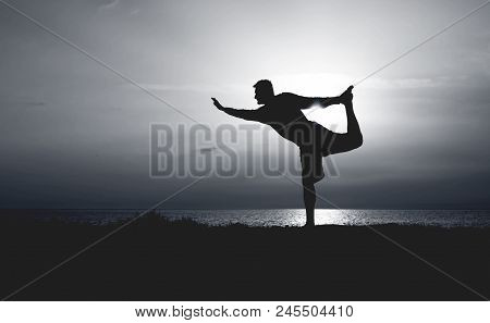 Silhouette Of Young Man Practicing Yoga. Sunset On The Seacoast. Standing Bow Pose Or Dandayamana Dh