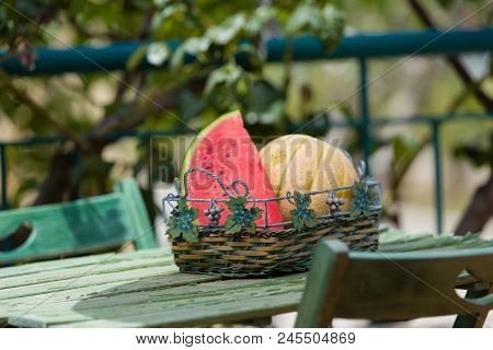 Seasonal Fresh Fruits, Watermelon And Rockmelon In Basket On Garden Table