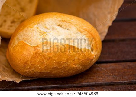 Fresh Baked Bread Wrapped In Paper, On Wooden Background