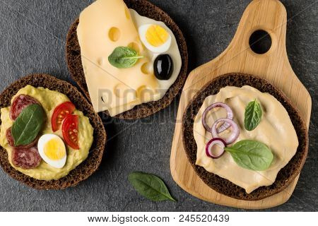 Open  faced  sandwich canape or crostini on a wooden serving board on dark stone background closeup. Top view.