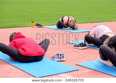 A Group Of Girls Performs Fitness Exercises In The Open Air. Exercise For Stretching In The Lotus Po