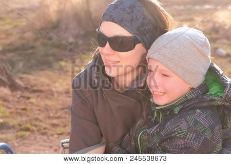 Mom And Son Look Around And Talk Sitting On A Bench In The Park In The Spring