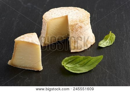 Crottin Cheese With Basil Leaves On Black Stone Background