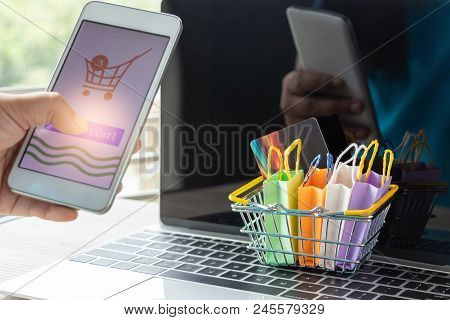 Hand Holding Smartphone With Add To Cart Icon. Colorful Shopping Bags And Credit Card In Basket On L