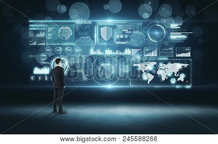 Back View Of Young Businessman Looking At Glowing Digital Business Interface. Innovation And Finance