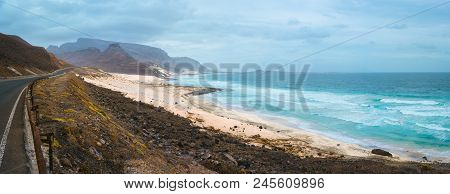 Road Along Atlantic Coastline White Sand Dunes And Ocean Waves Rolling. Road Leads Between Black Vol