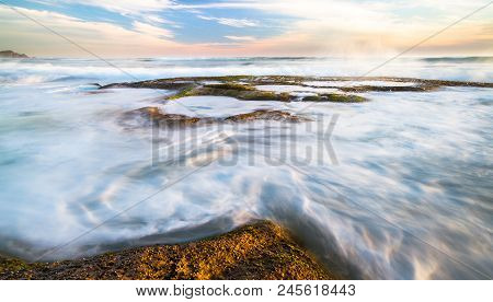 Long Exposure Of Ocean Waves Flowing Over Rocky Tidepools At Sunset On Johanna Beach In The Great Ot