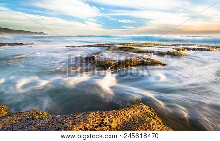 Long Exposure Of Ocean Waves Flowing Over Rocky Tidepools At Sunset On Johanna Beach In The Great Ot