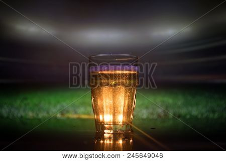 Creative Concept. Pint Of Fresh Beer On Grass Blurred Stadium On Background With Fog And Light. Glas