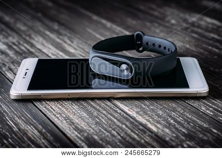 Black Fitness Tracker On White Smartphone On Wooden Table. Closeup, Selective Focus
