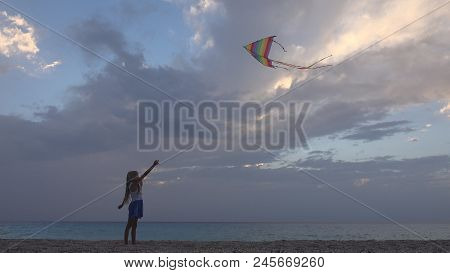 Child Playing Flying Kite On Beach At Sunset, Happy Little Girl On Coastline