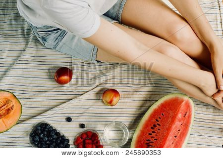 Summer Picnic Setting. Woman In Jean Shorts And Hat Eatining Water Melon, Melon, Blueberries, Raspbe