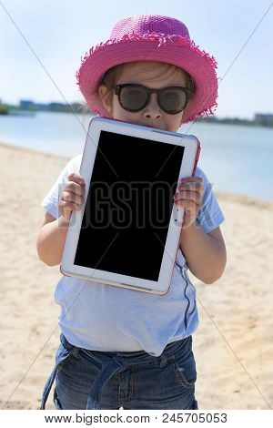 Little Girl With A Tablet Computer In Hands. Good Summer Weekend On The Beach. Copy Spce.