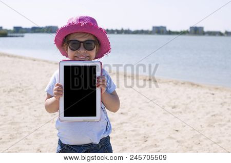 Little Girl With A Tablet Computer In Hands. Good Summer Weekend On The Beach. Copy Spce