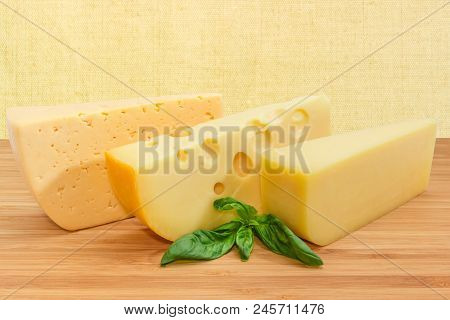 Pieces Of The Medium-hard Cheese, Swiss-type Cheese And Hard Cheese With Green Basil Twig On Bamboo 
