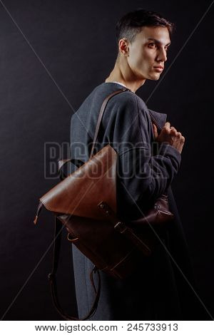 Studio Shot Of A Handsome Young Male Model Wearing Dark Topcoat And Brown Lether Beg Over His Should
