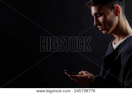 Profile Of Serious Concetrated Man Using Smartphone On Dark Background With A Lot Of Copyspace.