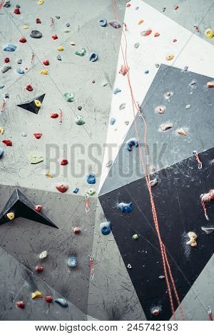 Grey Surface Of An Artificial Rock Climbing Wall With Toe And Hand Handles And Hooks Studs.