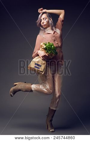 Stylish Woman In Biofuture Pompadour Style. Female In Fashion Cloths And The Green Plant In Paper Ba