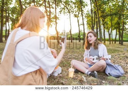 Girl Takes The Girl's Ukulele At The Camera. Shooting A Cover On Ukulele. The Two Girls Sit In The P