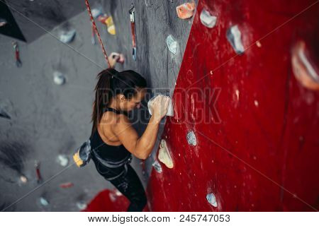 High Angle View Of Professional Sport Female Rock Climber On Red Vertical Wall Preparing To Competit