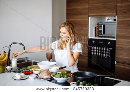 Smiling Caucasian Woman Making Healthy Meal And Reading Message At Phone In The Domestic Kitchen.